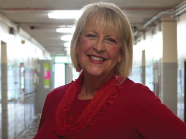 woman with shite shoulder length hair smiling at camera wearing a red sweater